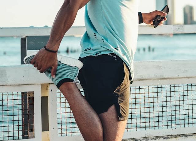 Hardloper doet dynamische warming-up oefening langs een parkpad